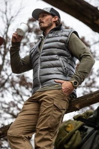 male wearing the Grumman Vest, holding a mug, and leaning on a wooden railing