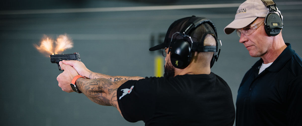 One person watching another shoot a handgun at an indoor gun range