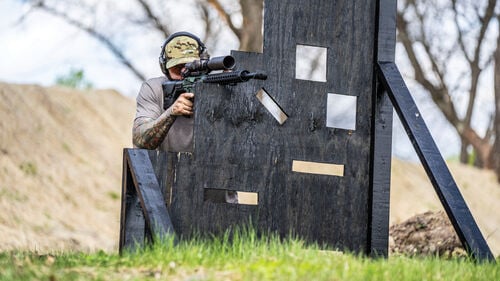 man aiming rifle that is rested on a course obsticle