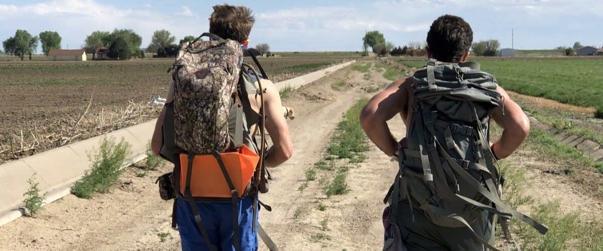 two men carring backpacks on a dirt road