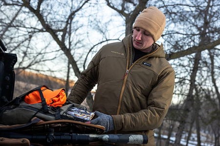 male wearing the Cirque jacket and getting ammo out of an ammo bag sitting on the tailgate of a pickup