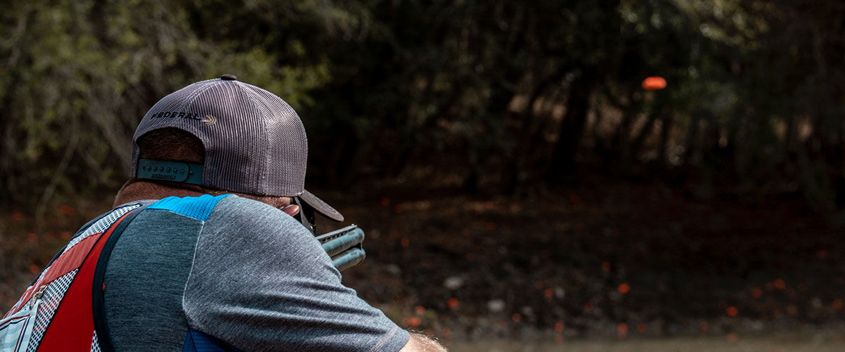 shooter aiming shotgun at flying clay pigeon