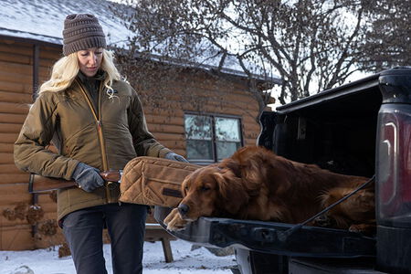 female wearing the Cirque jacket and getting a rifle out of a gun case in the bed of a truck with a dog laying on the tailgate