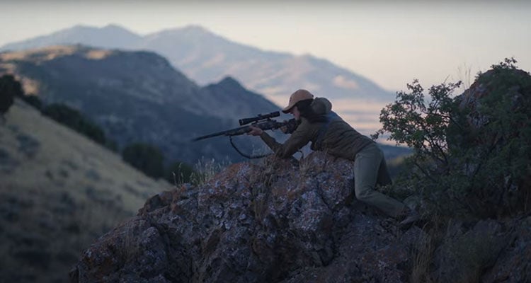 female hunter using a large boulder to steady her rifle